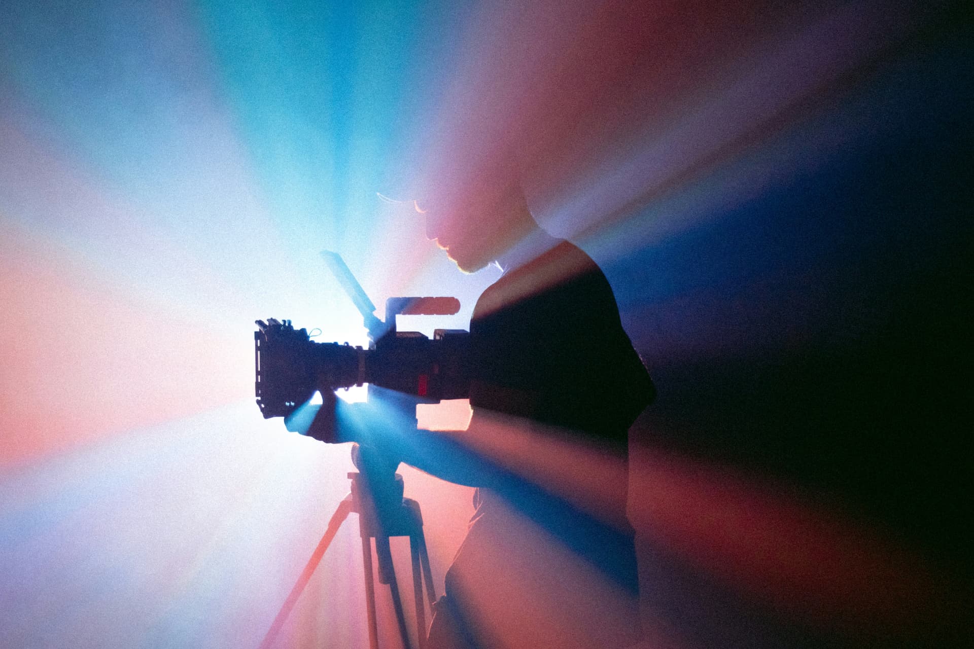 A camera operator silhouetted against rays of light behind the lens