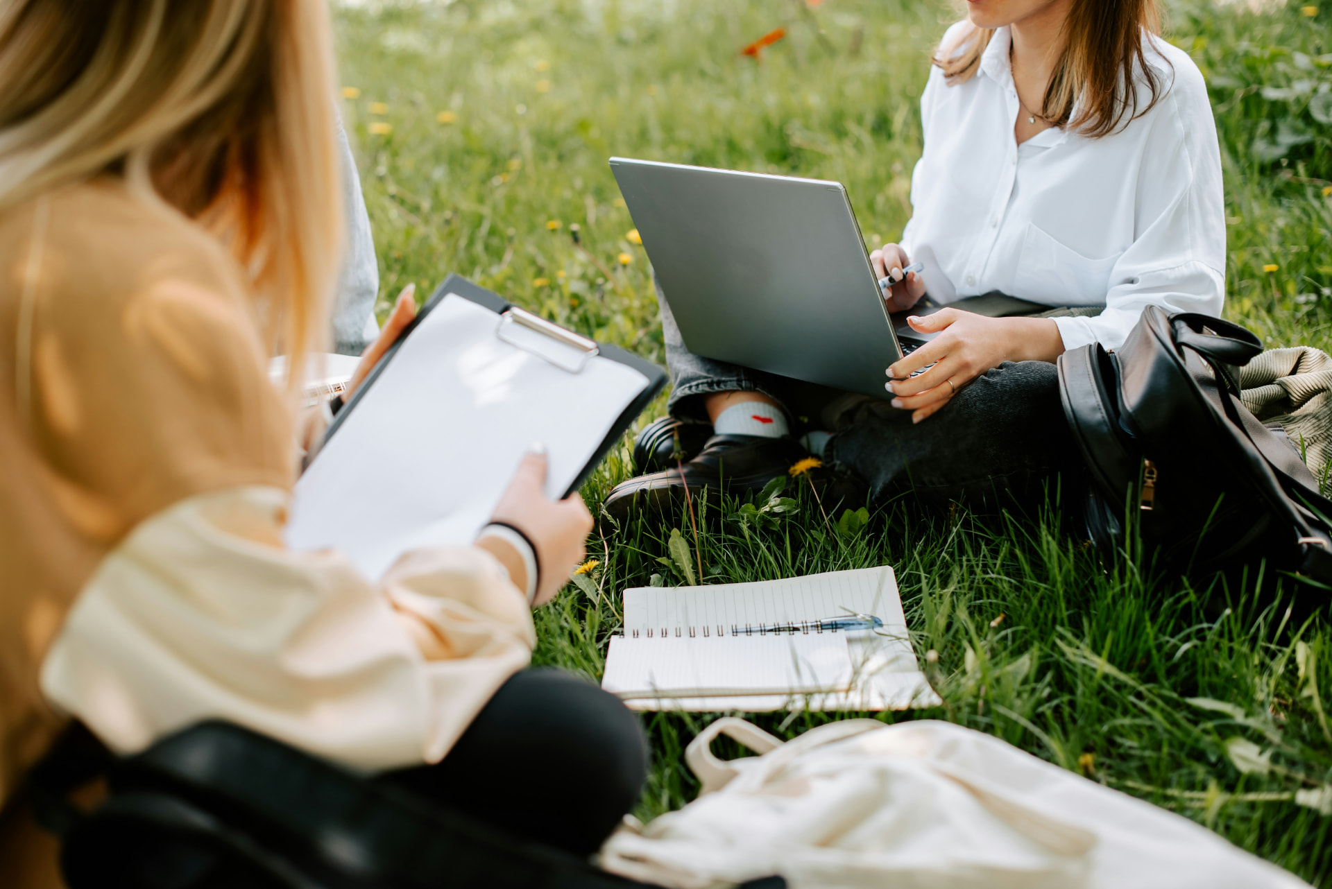 Two people working through plans outdoors with a laptop, notebook and paperwork on the grass